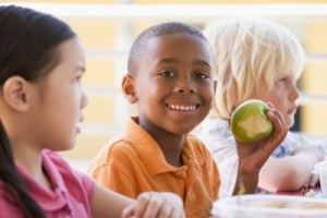 picture of african american boy eating apple at school lunch with peers